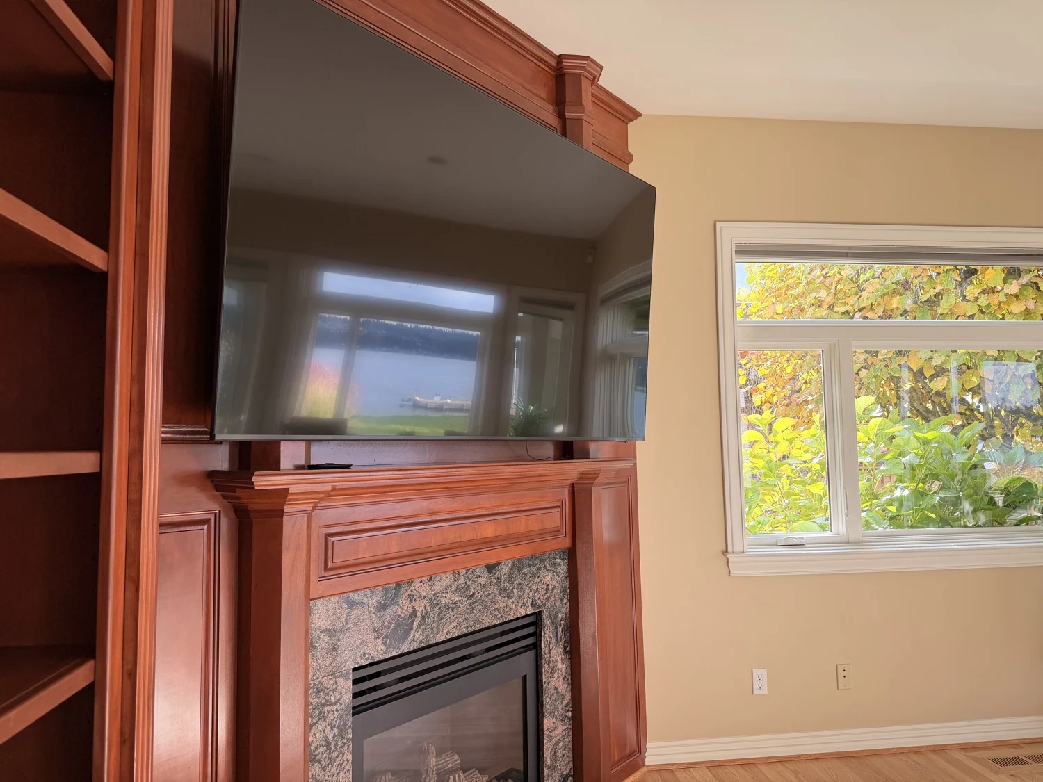 Wall-mounted TV over a fireplace with a lake view reflected in the screen, Sammamish