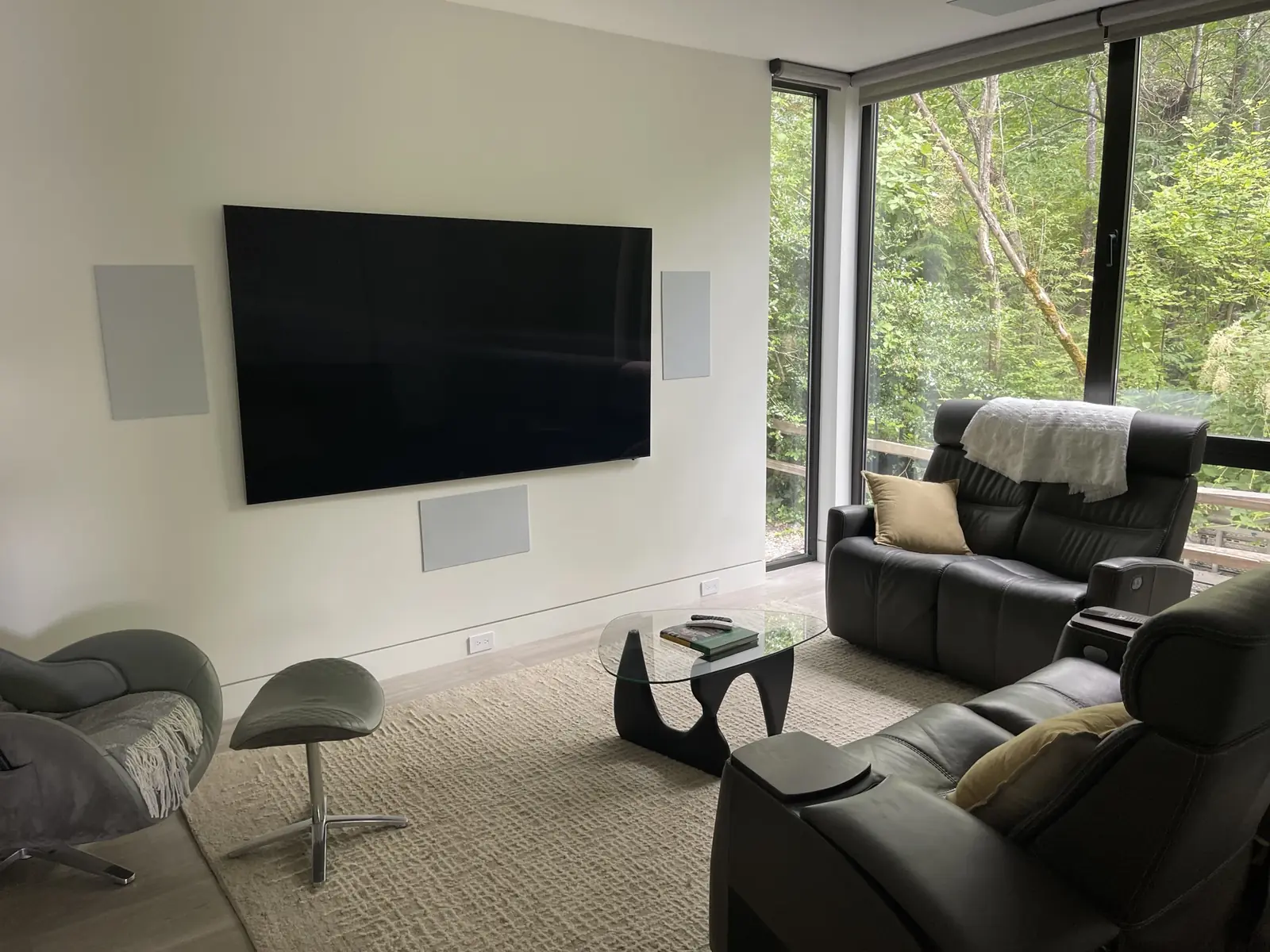 Sammamish media room with a wall-mounted TV, in-wall speakers and recliners facing a forest view