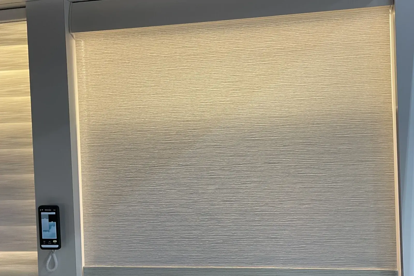 Glowing backlit window panel behind a roller shade, with a wall control beside it